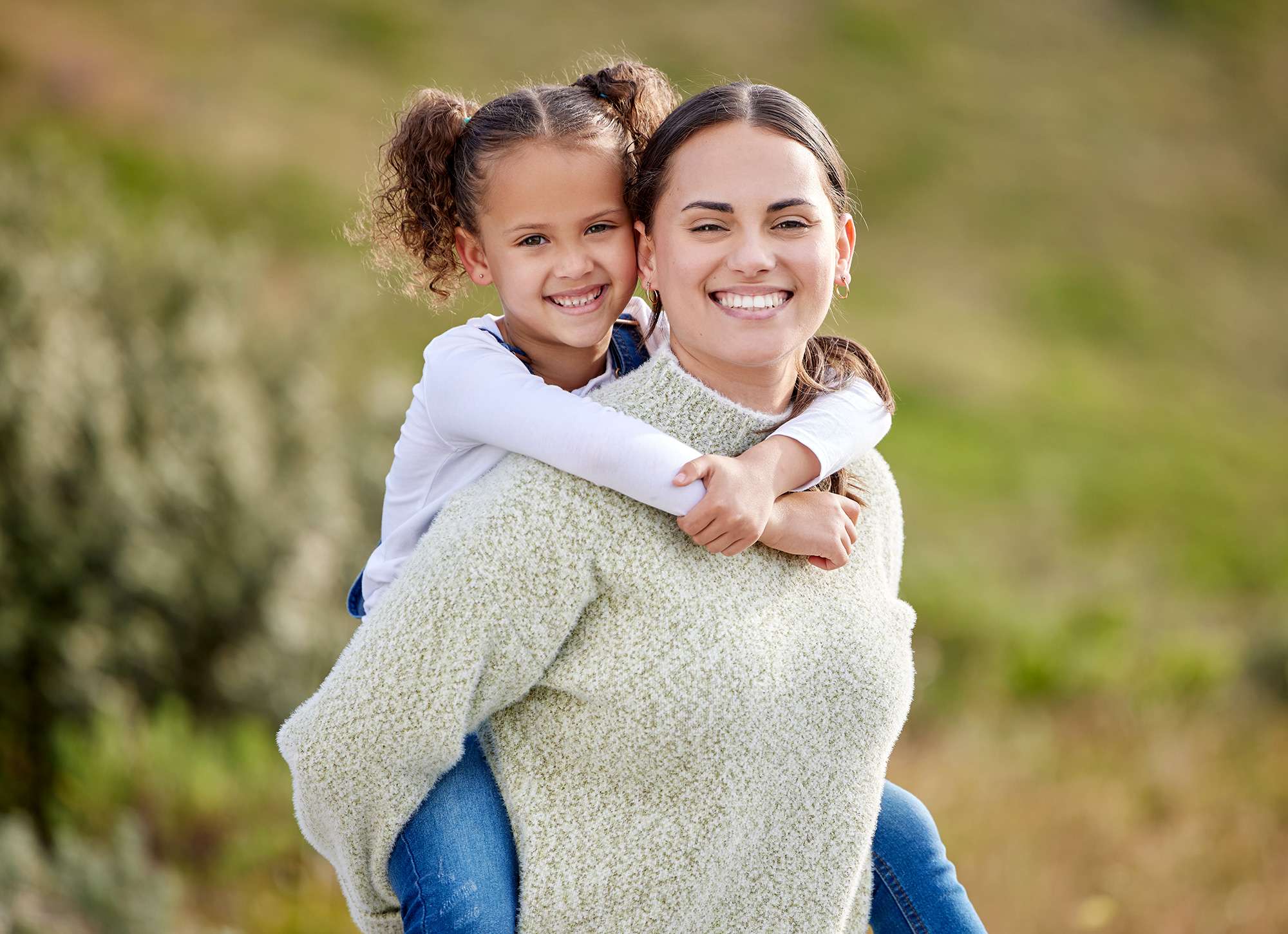 A smiling mother and daughter, mother holding her daughter on her back, an image paired with a blog on surgeon patient relationship for surgery