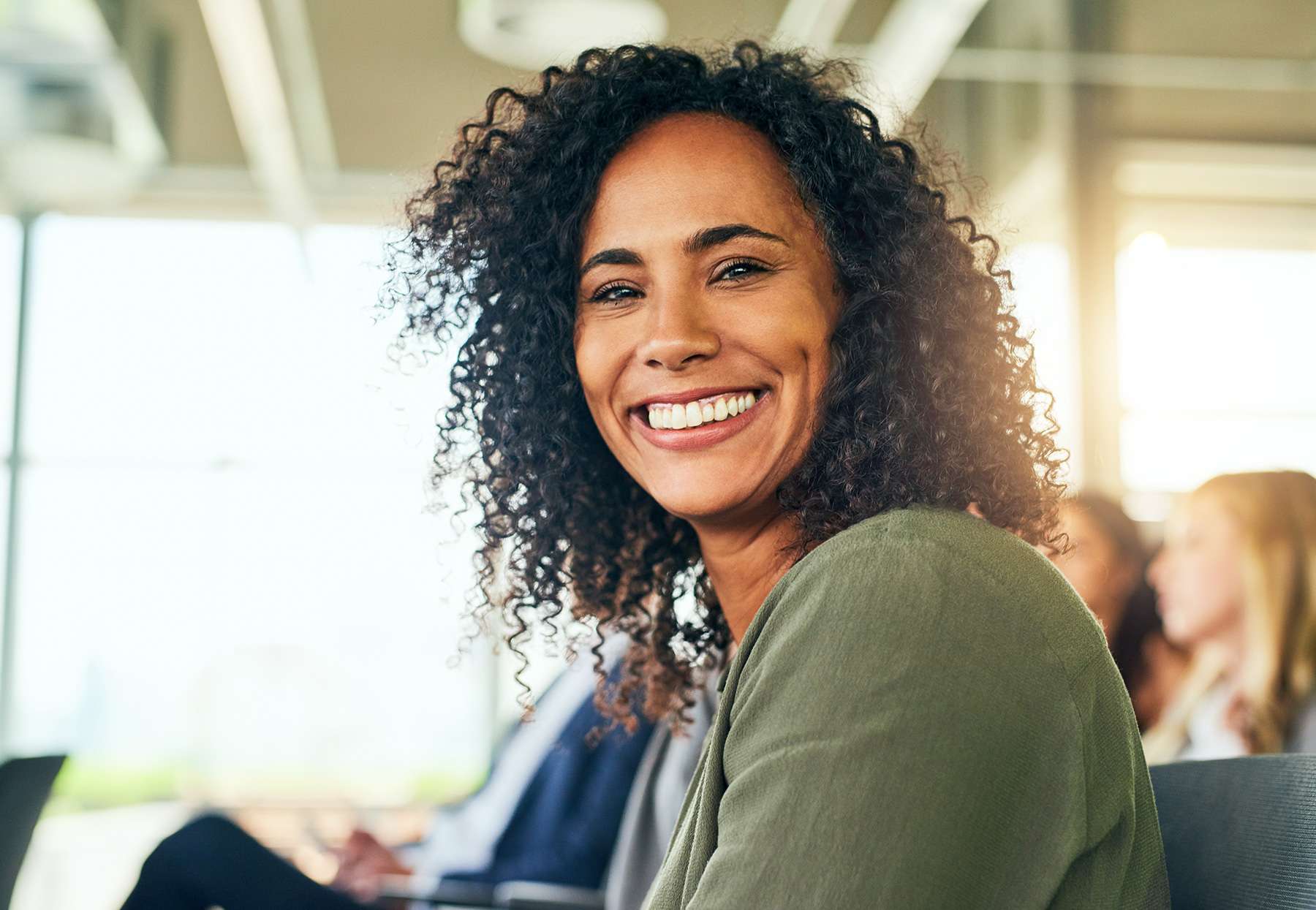 A woman smiling directly at the camera, two people sitting behind her, an image paired with a blog on gastric sleeve surgery